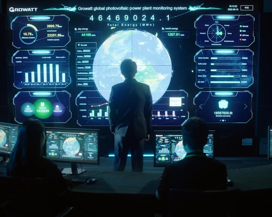 A person in a suit stands before a digital display monitoring global photovoltaic power plant data, with two colleagues at computers.